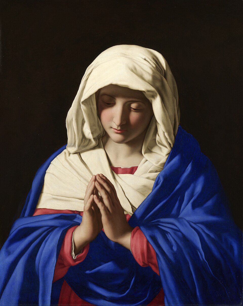Painting of the Virgin Mary with her head veiled in blue, eyes lowered and hands joined in quiet prayer against a dark ground.